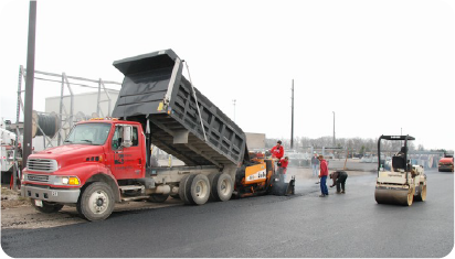 Commercial paving crew installing new asphalt parking lot with dump truck, paver, and roller in Delaware, Ohio.