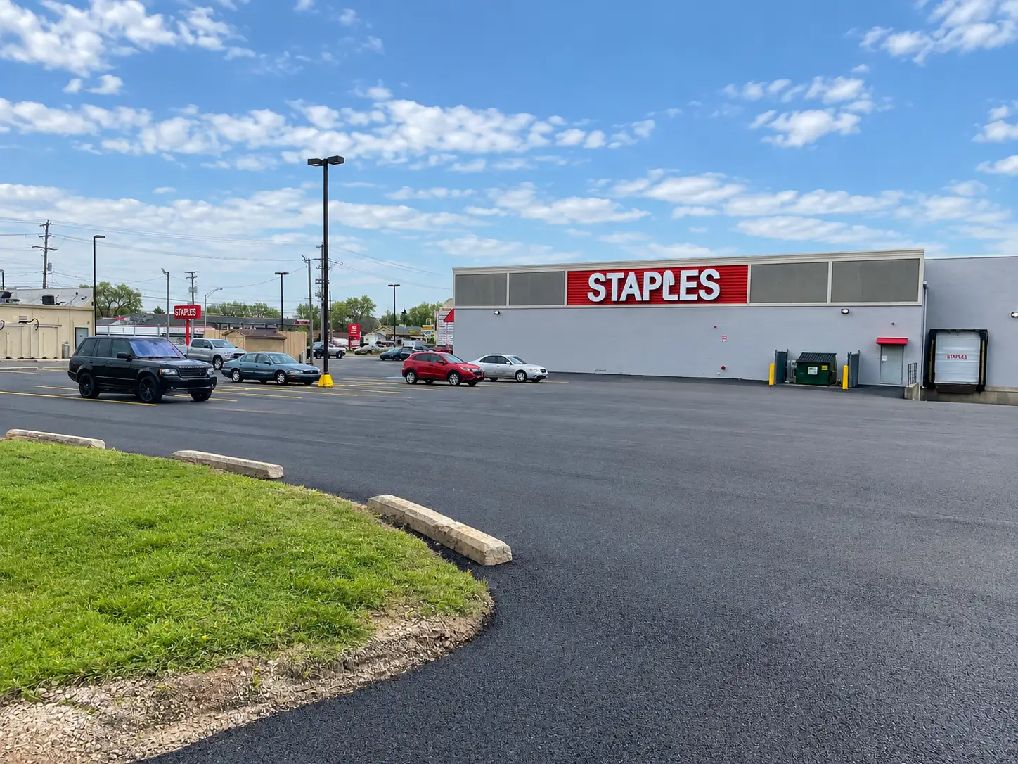 Freshly paved asphalt parking lot behind a retail store with new curb stops along a grass island