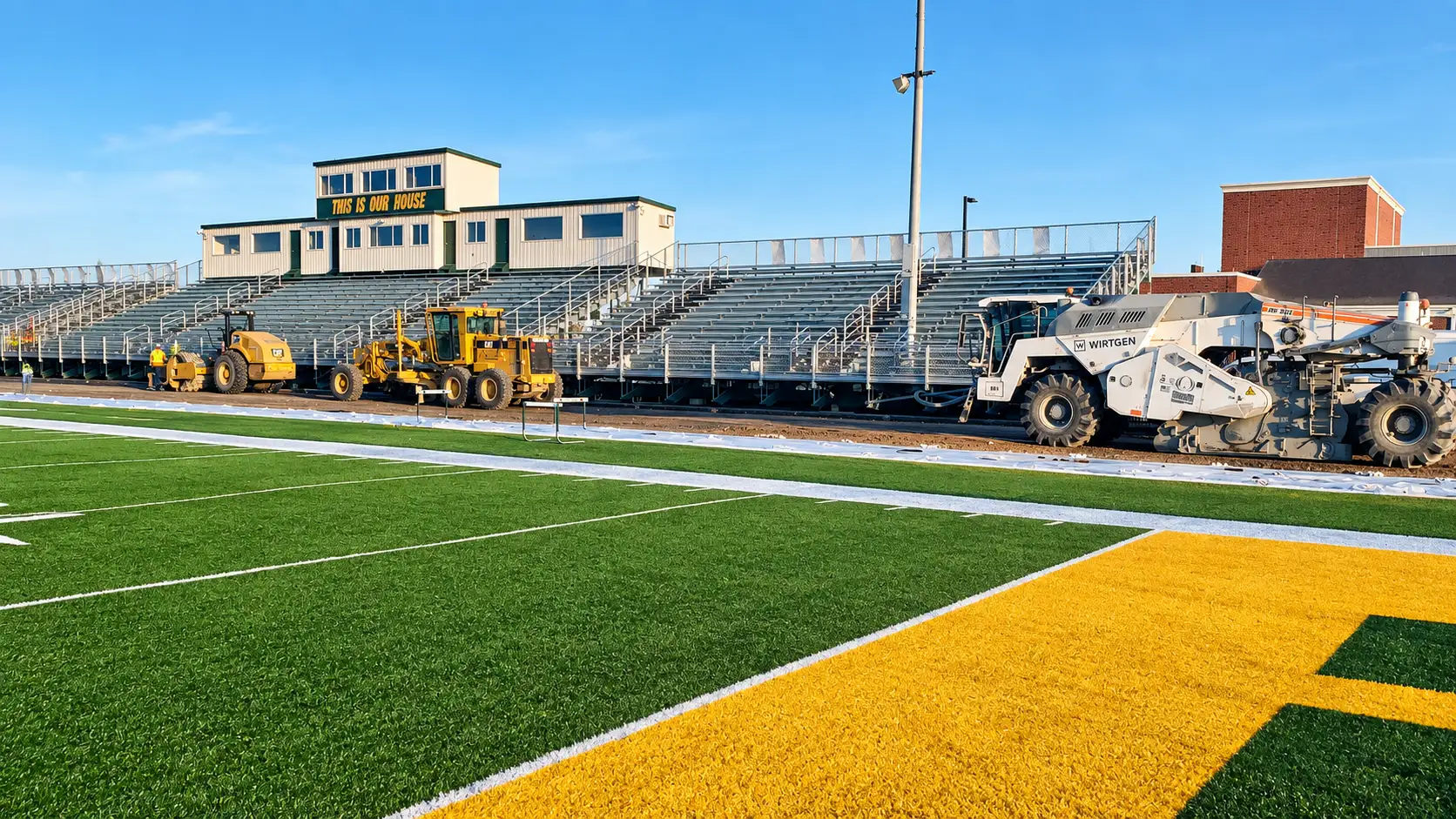 Grading and reclamation equipment preparing the track surface beside a high school football field